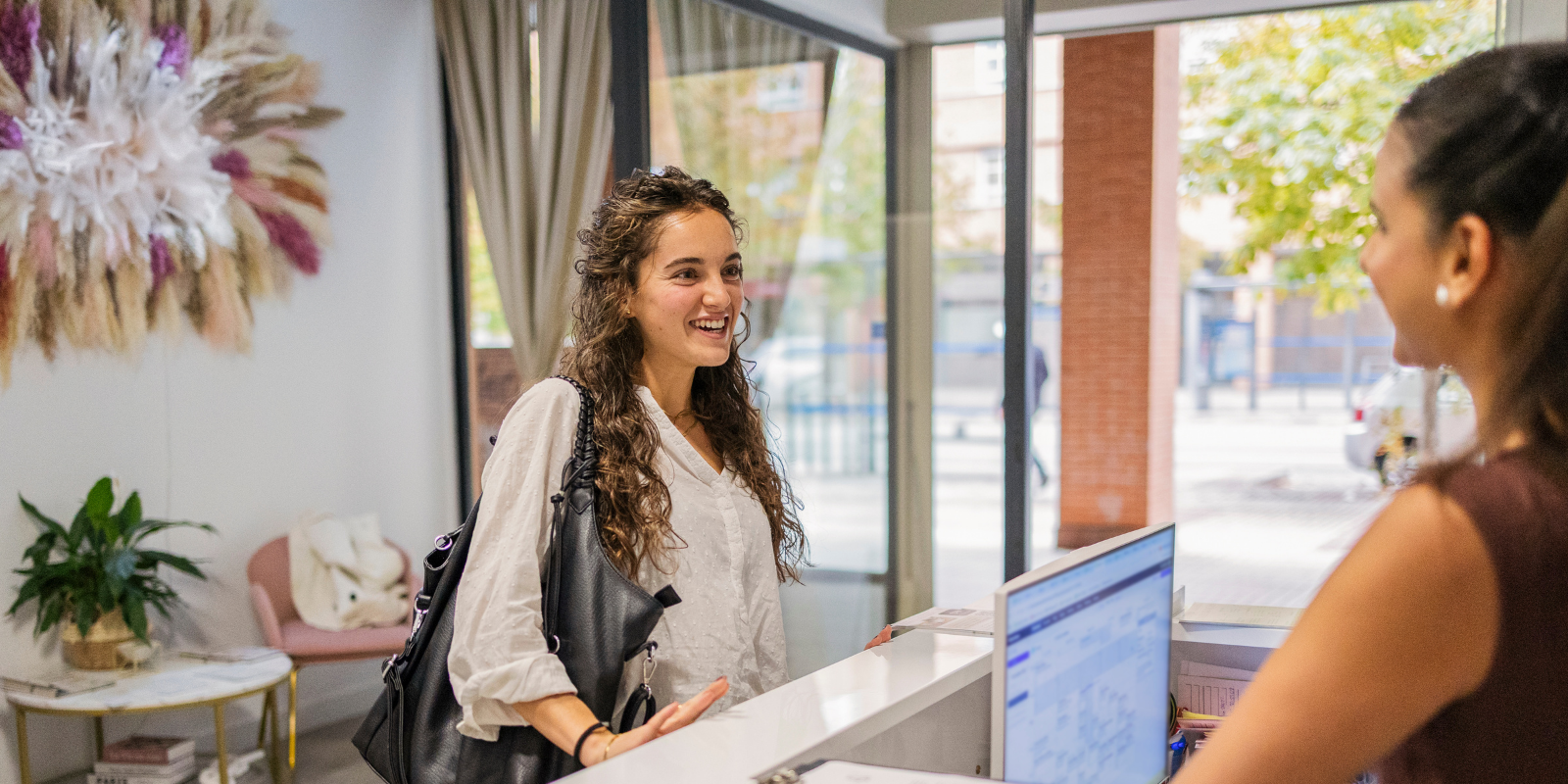 Two women talking across a reception desk in a bright, modern office lobby