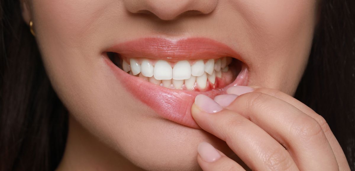 Close-up of a smiling mouth as fingers hold a dental floss thread between the teeth
