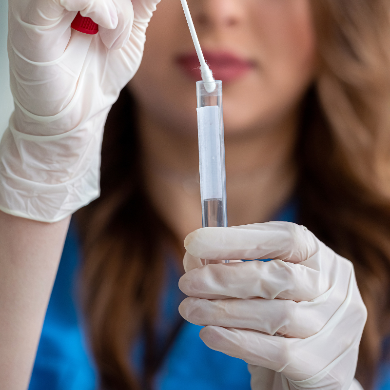 Gloved hands holding a test tube with a cotton swab in a lab setting