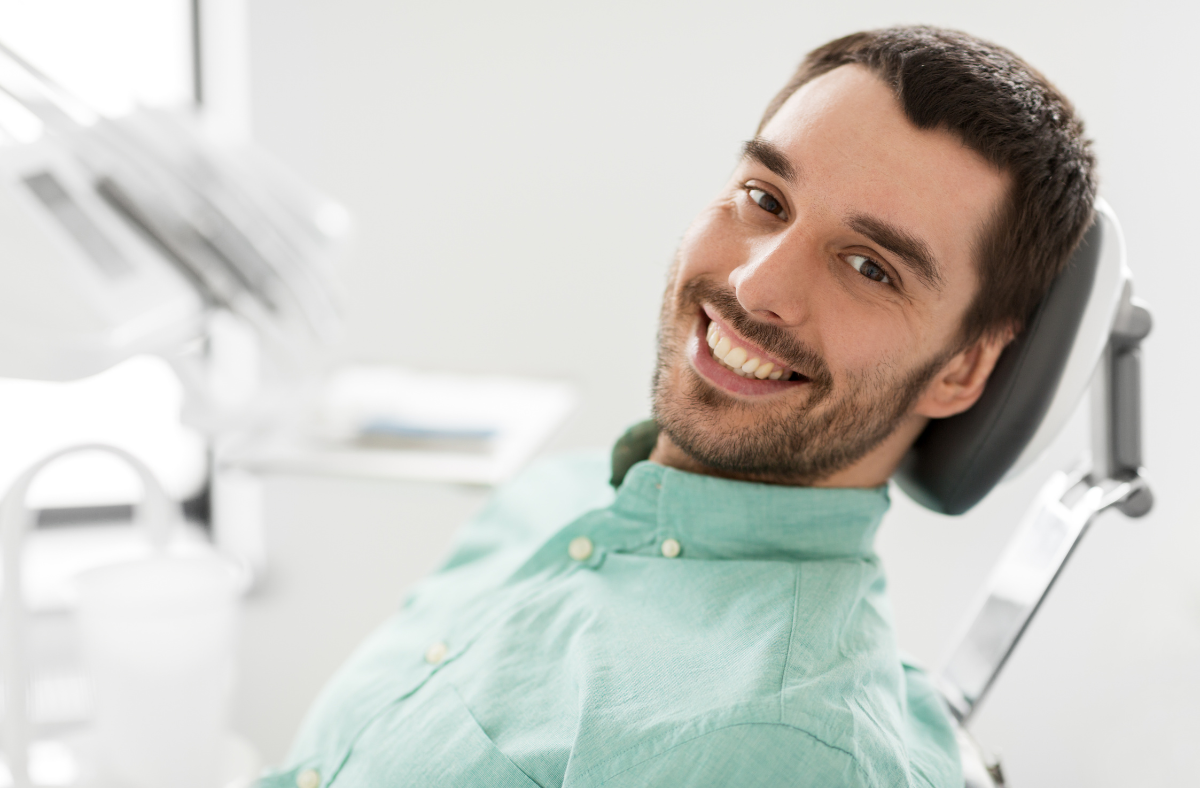 Man smiling in a dentist's chair, wearing a light green shirt, in a dental office.