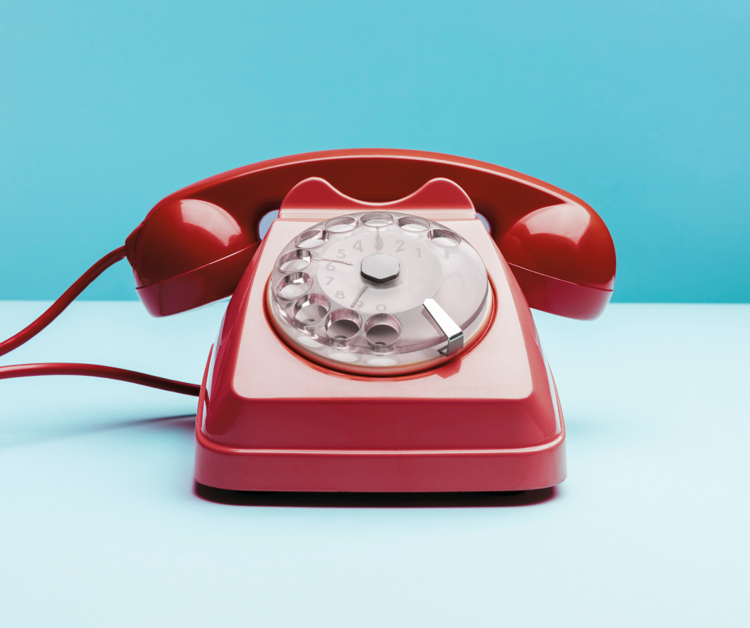 Red rotary phone on a light blue surface against a blue backdrop.