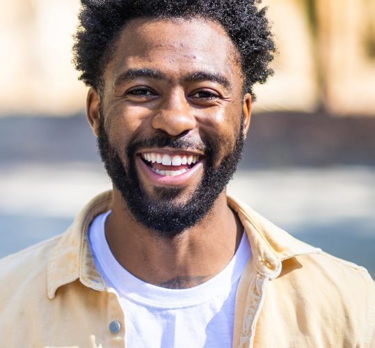A man with a beard is smiling and wearing a tan shirt