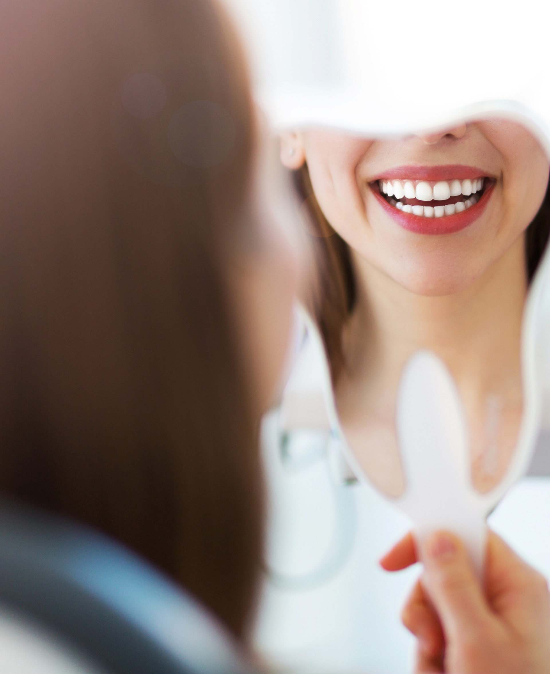 Woman smiling while looking at her teeth in a hand-held mirror.