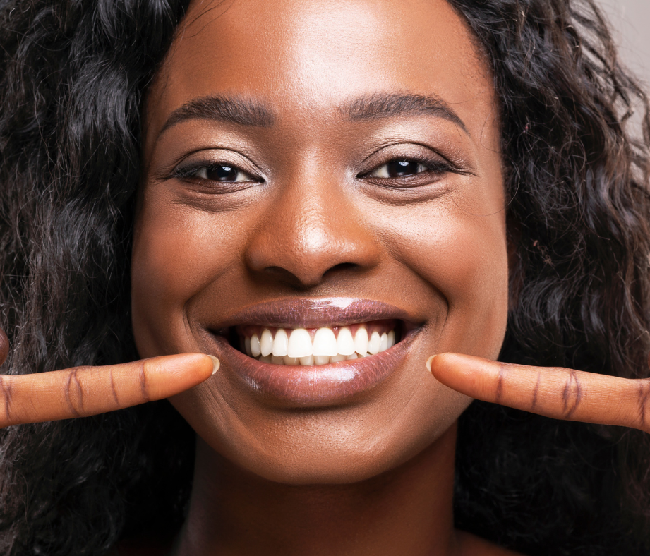 Woman with curly hair smiling and pointing at her teeth.