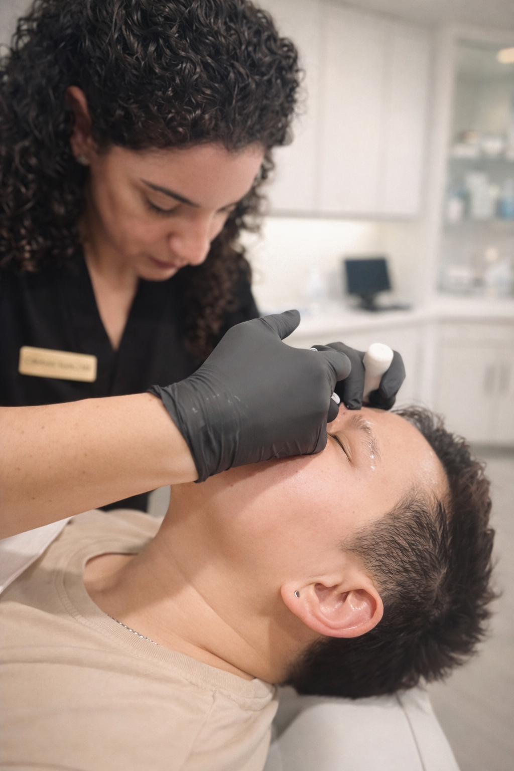 A medical professional in a black top and gloves performs an aesthetic procedure on the forehead of a patient.