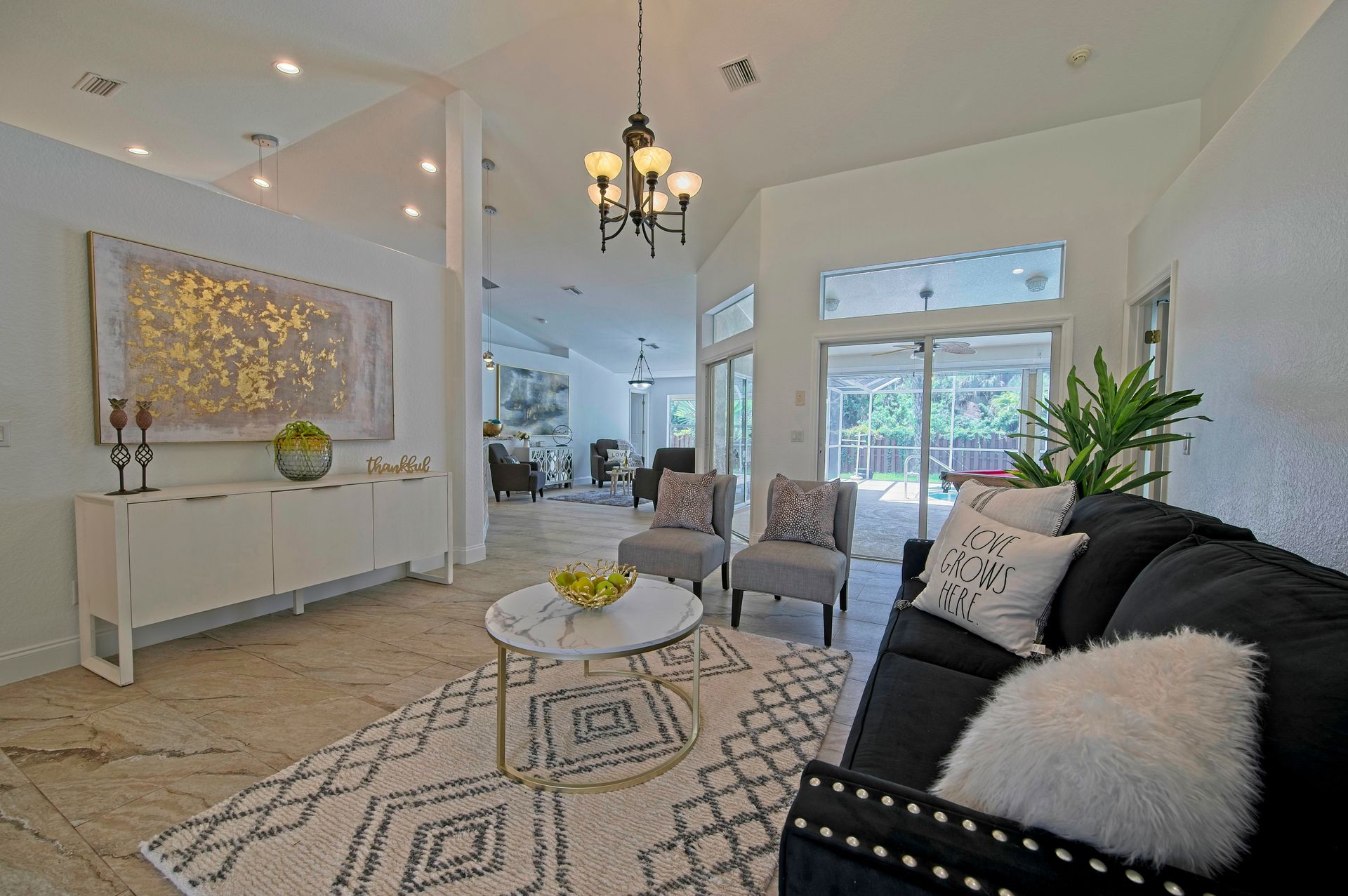 Bright living room with white walls, black sofa, two gray chairs, and decorative rug.