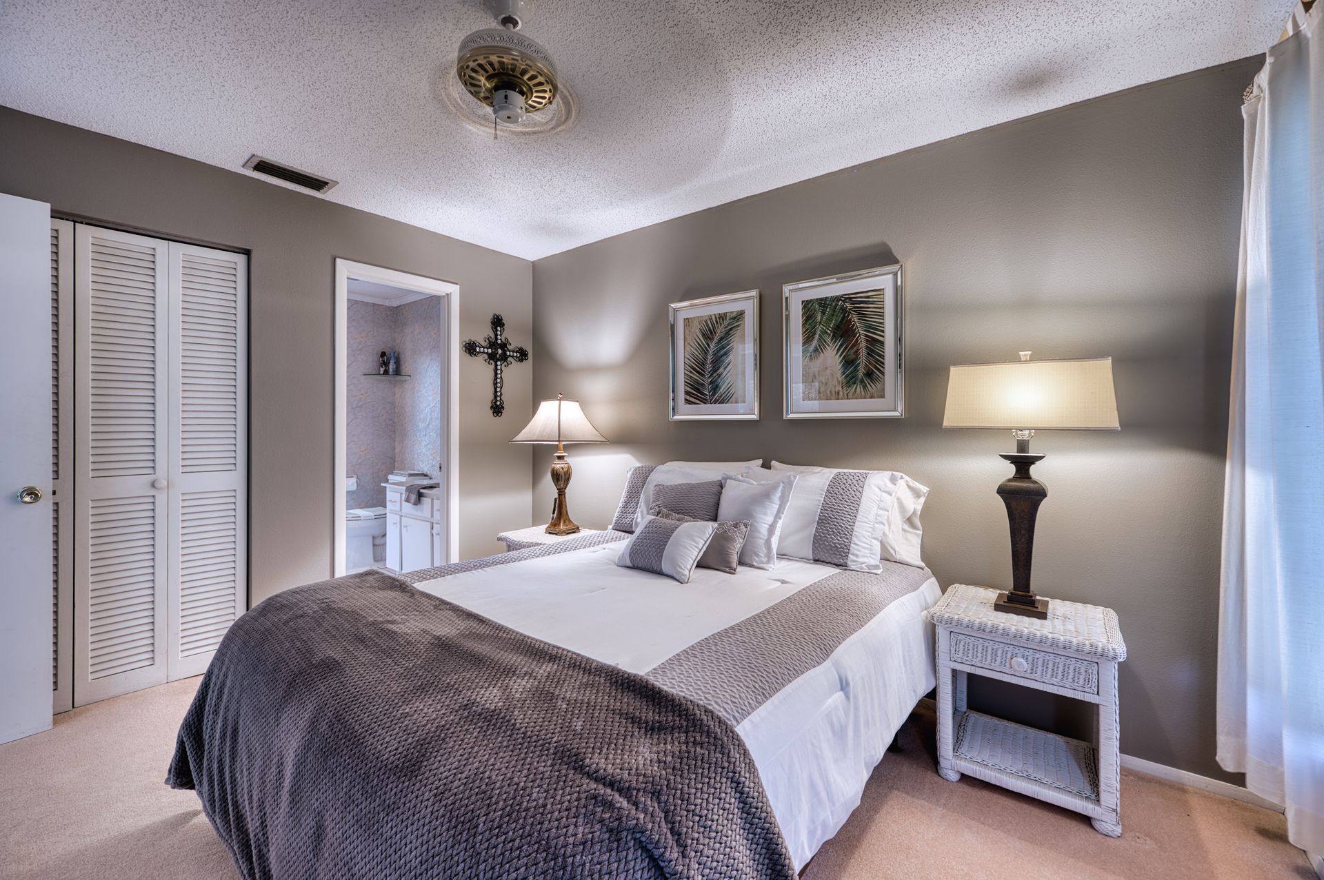 Bedroom with bed, nightstands, lamps, artwork, and a partially visible bathroom.