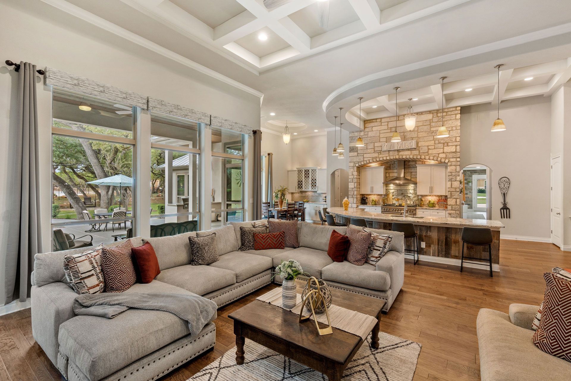 Spacious living room with sectional sofa, coffee table, and open kitchen with stone backsplash and wood floors.
