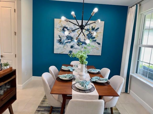 Dining room with teal accent wall, wooden table, white chairs, and modern light fixture.
