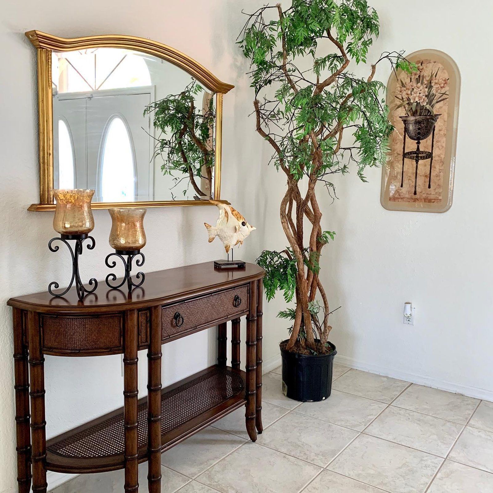 A foyer with a wooden console table, mirror, plant, and wall art; tan, brown, and gold tones.