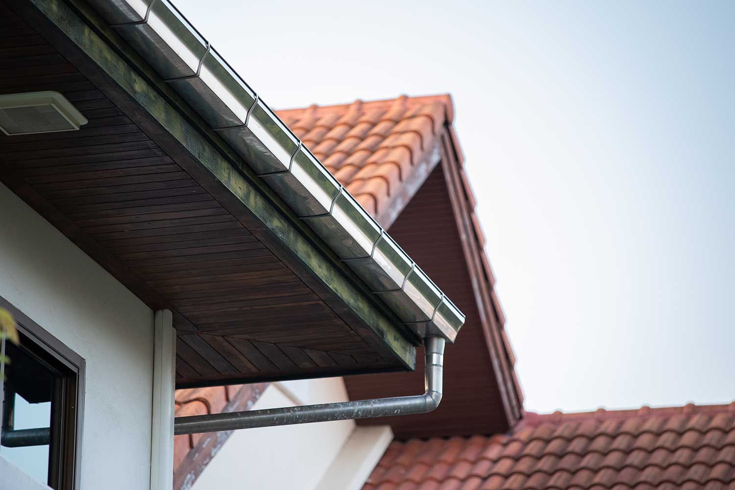 En tagrende på siden af ​​et hus med rødt tegltag.