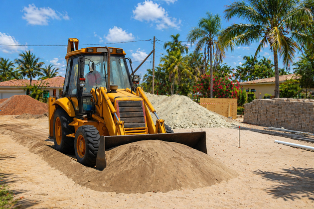 Orange excavator digging in a grassy yard near a brick house.
