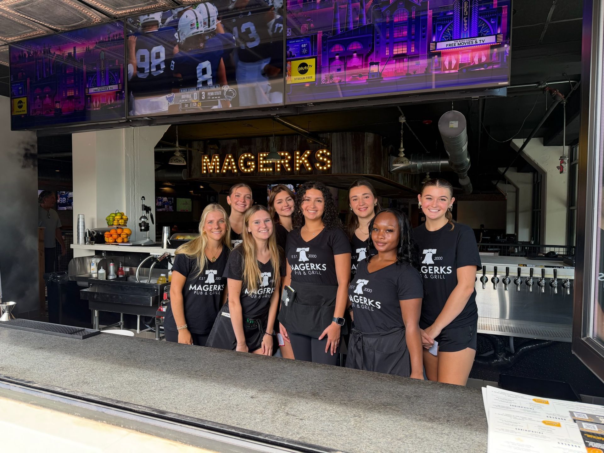 Busy sports bar with patrons eating and watching TVs. Servers walk among tables. Wooden bar and floors.