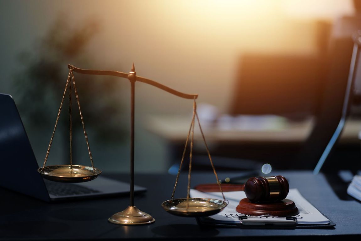 Brass scales of justice beside a gavel on a desk in warm office light