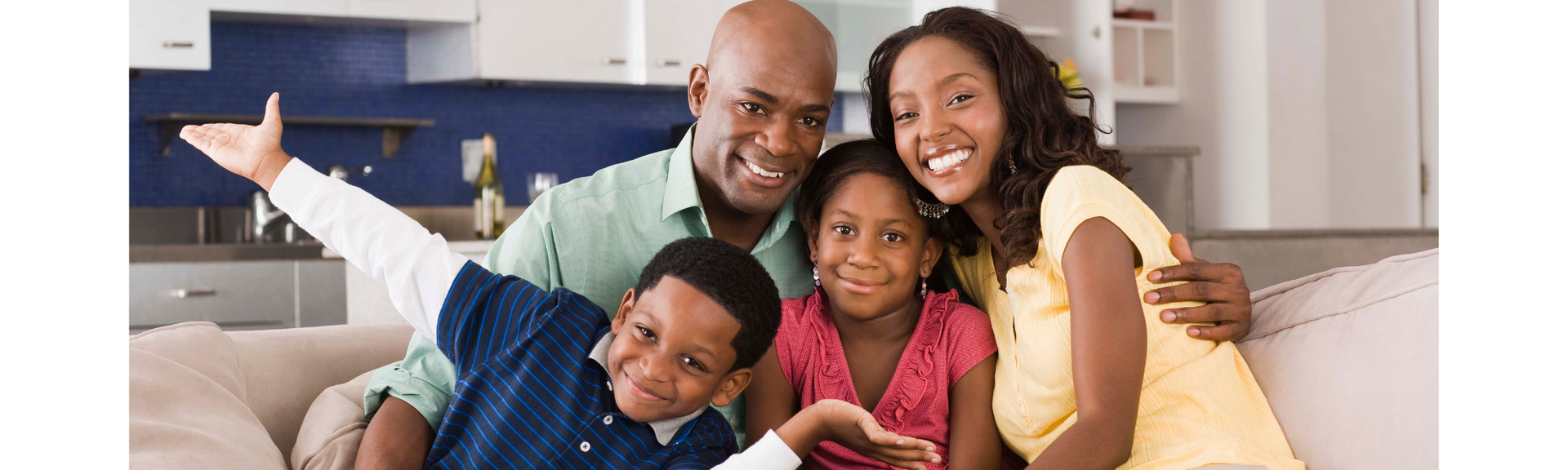 Family smiling on a couch, with children in front and a white dog beside them.