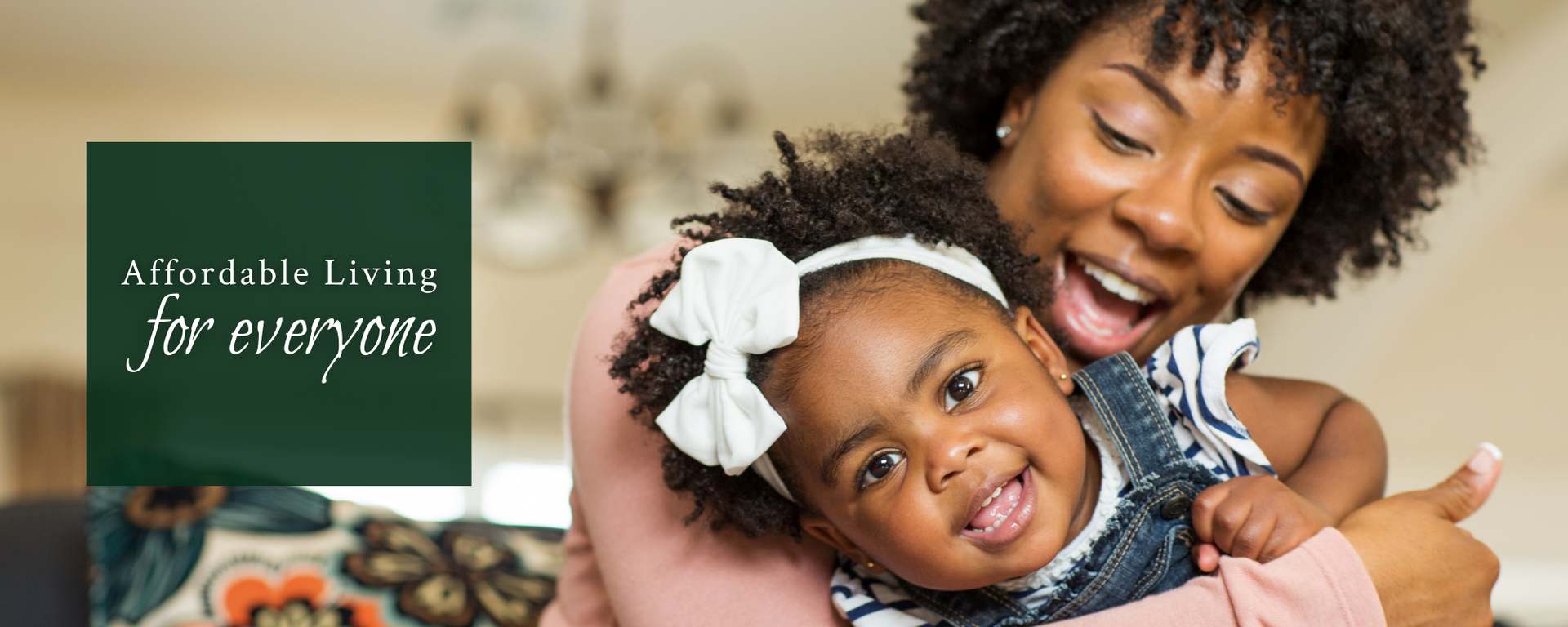 Smiling adult holding a laughing baby beside a green panel reading “Affordable living for everyone”