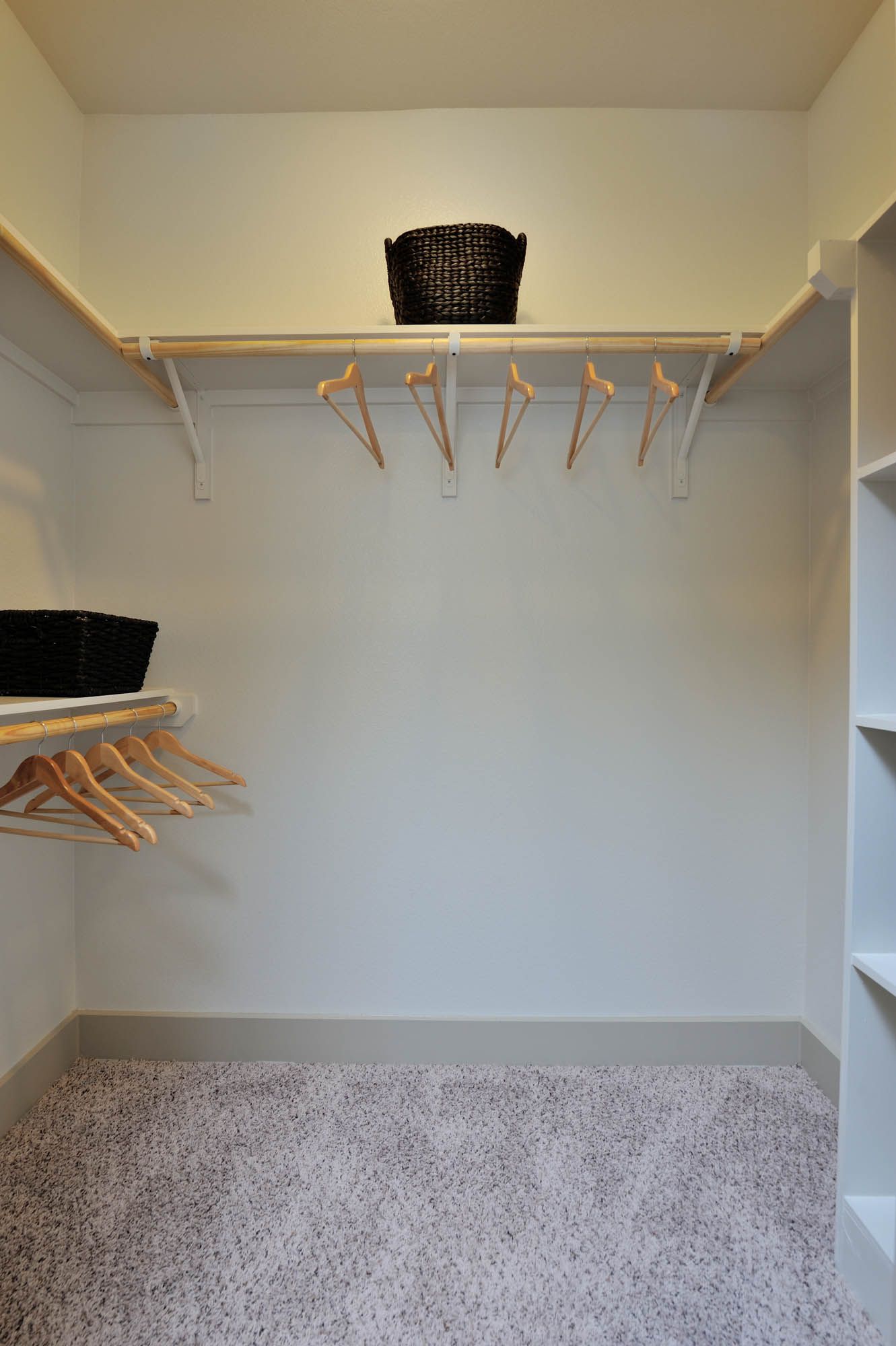 Walk-in closet with hanging rods, shelves, and woven baskets.