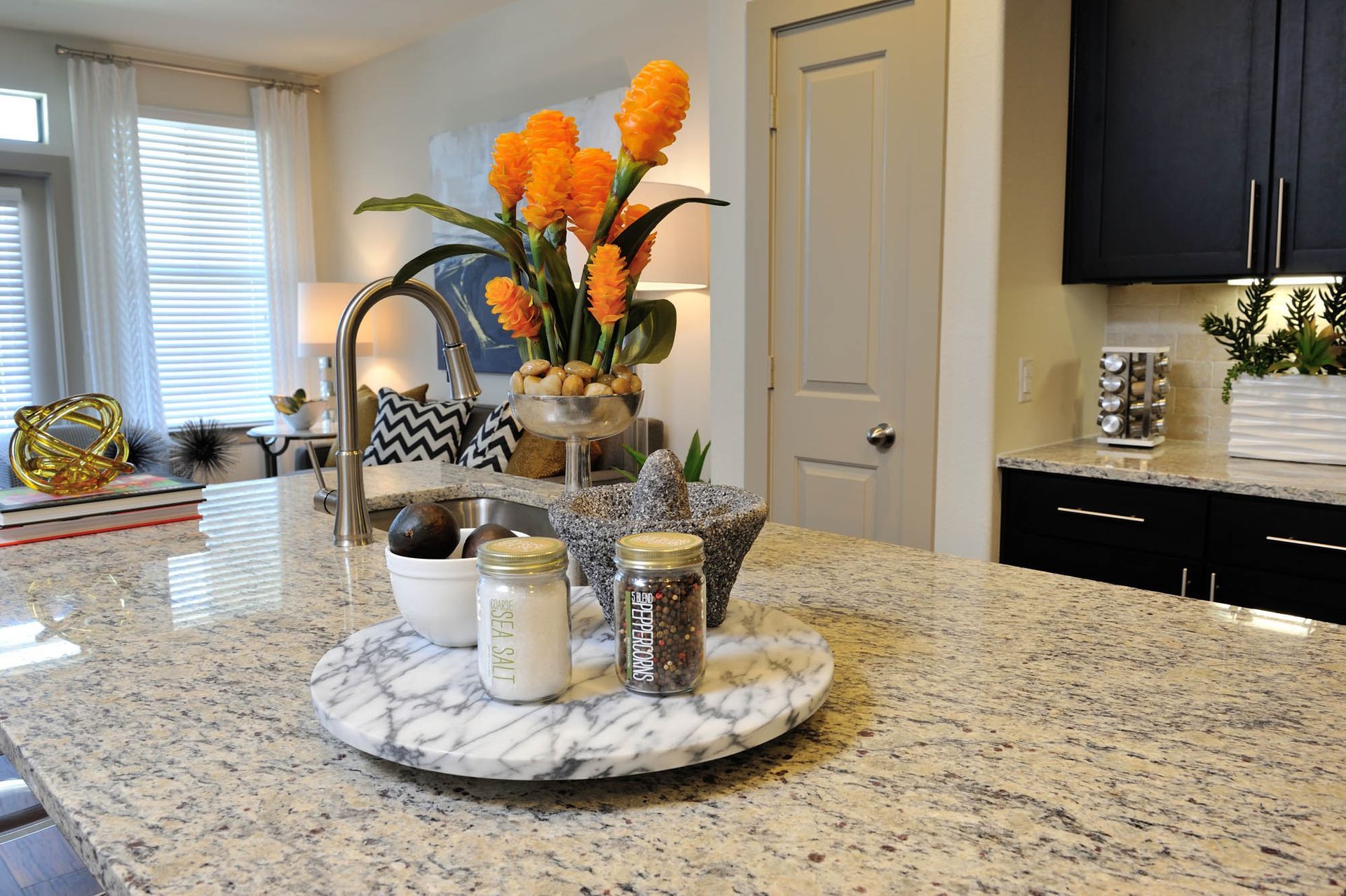 Modern apartment kitchen with granite island, sink, and orange flower arrangement.