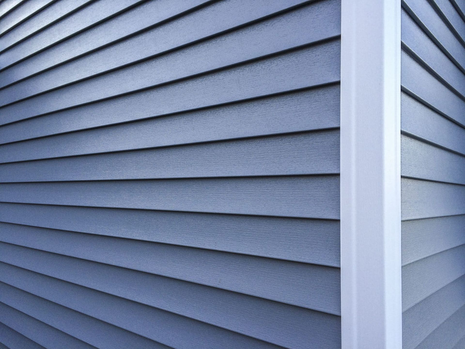 Blue horizontal vinyl siding on a building corner with a white vertical corner trim piece.
