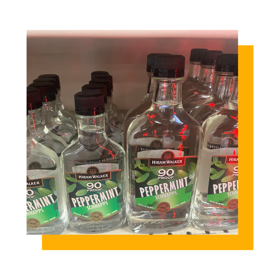 Mini bottles of peppermint schnapps on a shelf; clear liquid, black caps, green and black labels.