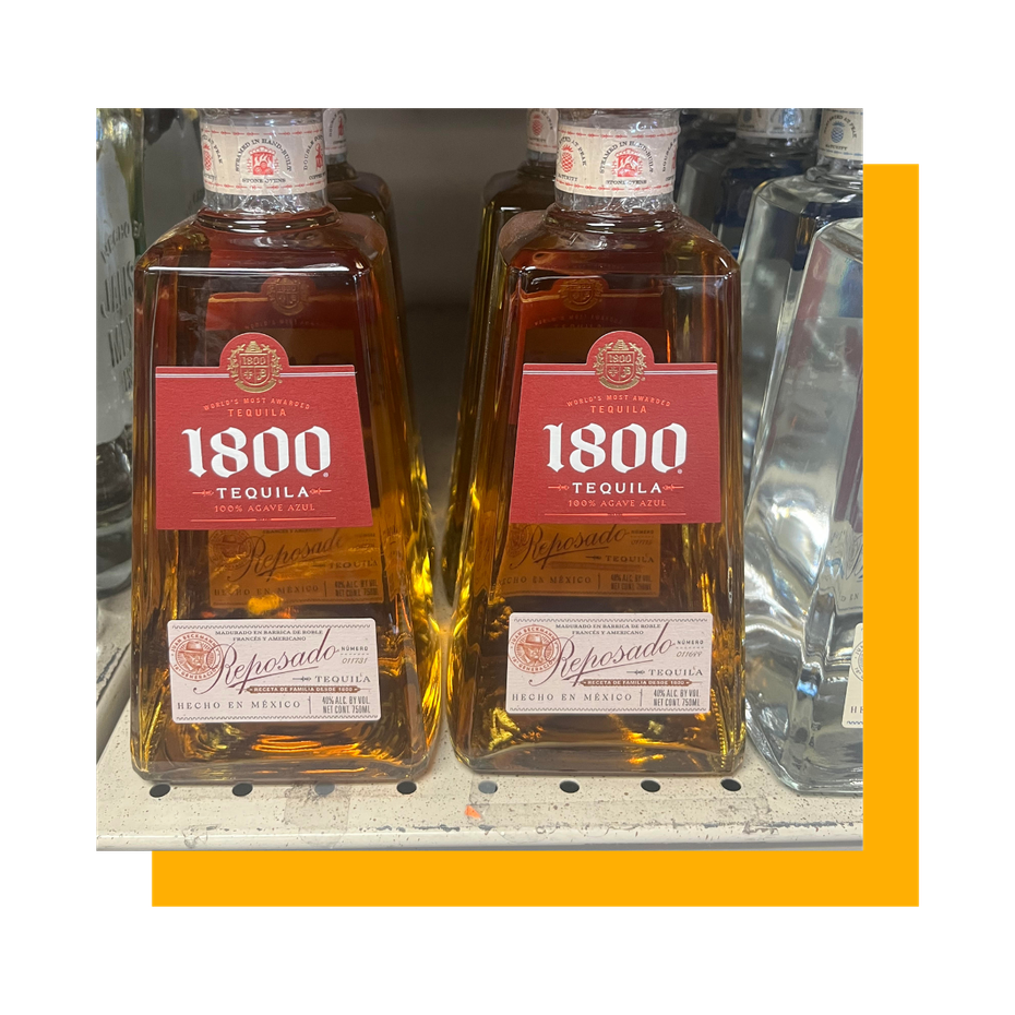 Two bottles of 1800 Tequila, amber liquor in square bottles, on a shelf.