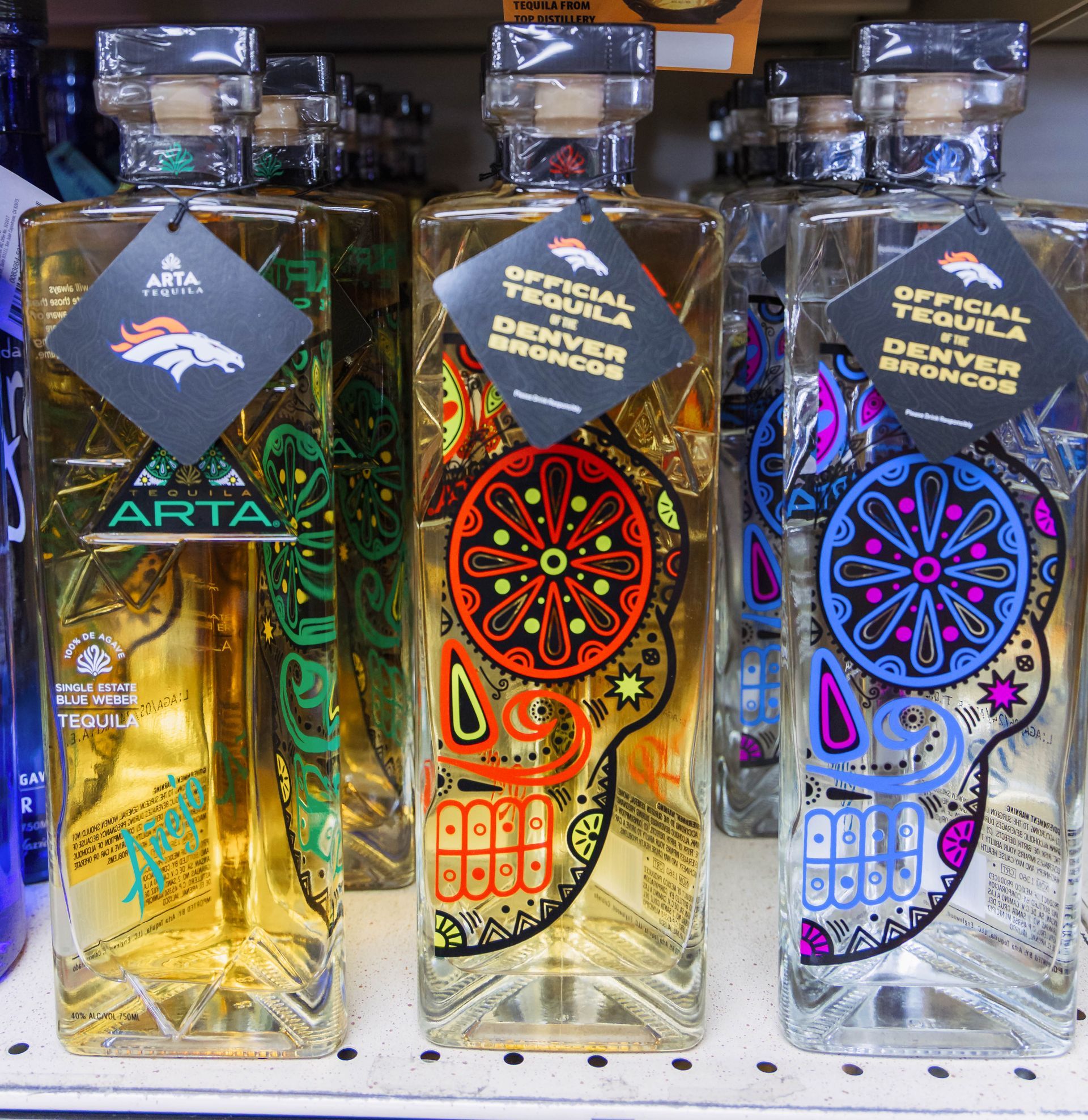Bottles of Arta tequila, official tequila of the Denver Broncos, with colorful skull designs.