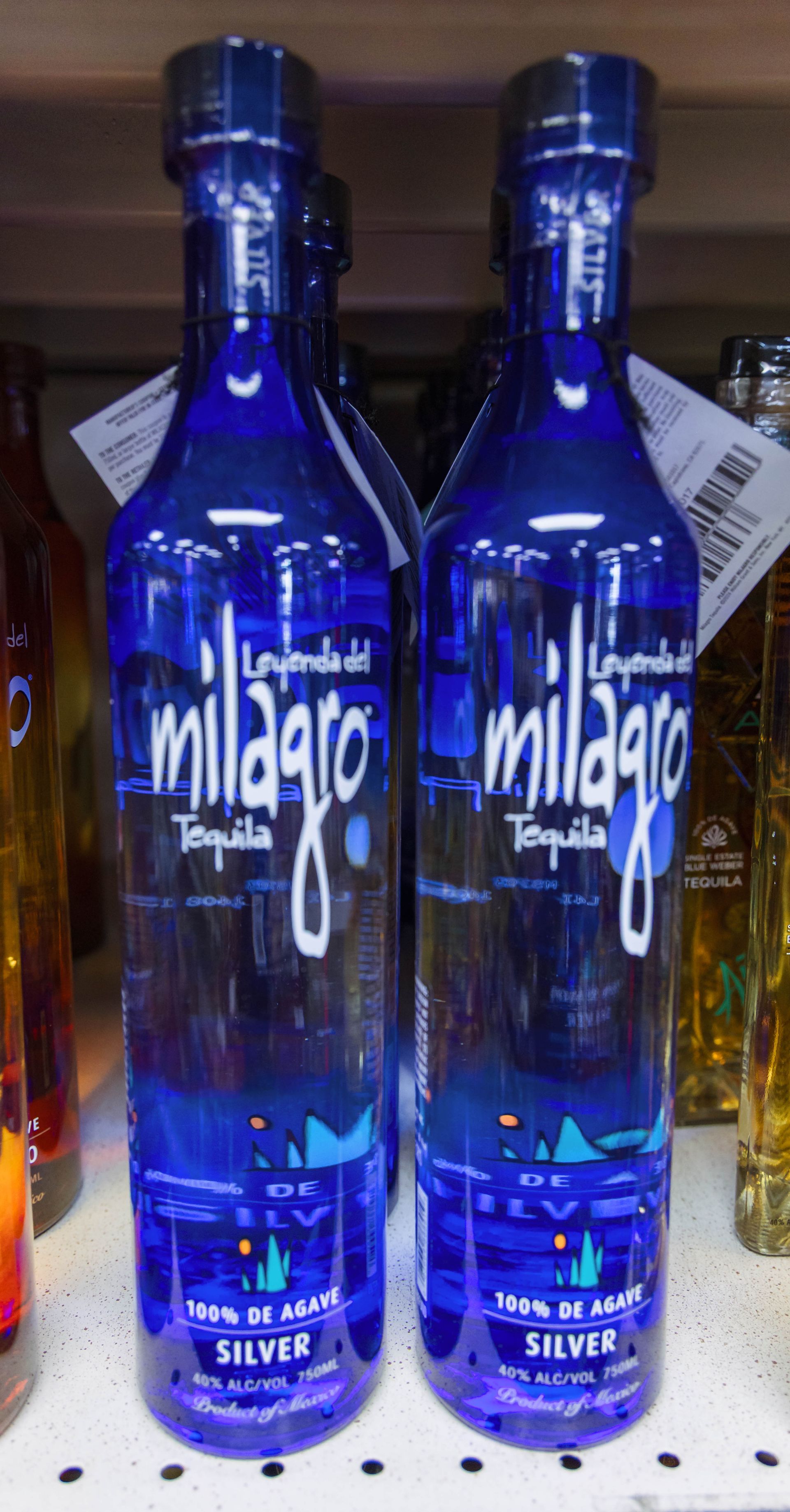 Two bottles of Milagro Silver tequila on a shelf. Blue bottles with white text, 