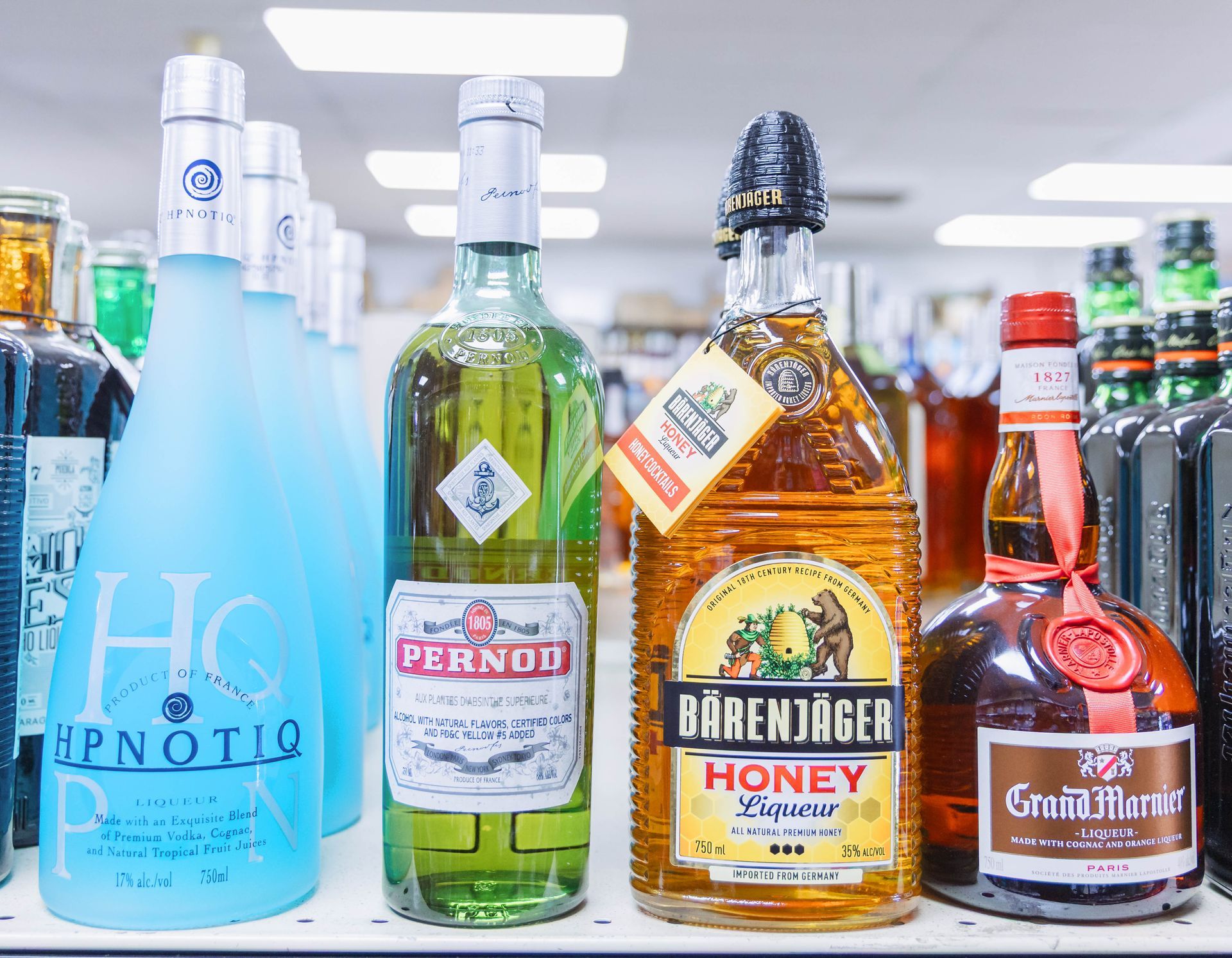 Liquor bottles on a store shelf: Hypnotiq, Pernod, Bärenjäger Honey, and Grand Marnier.