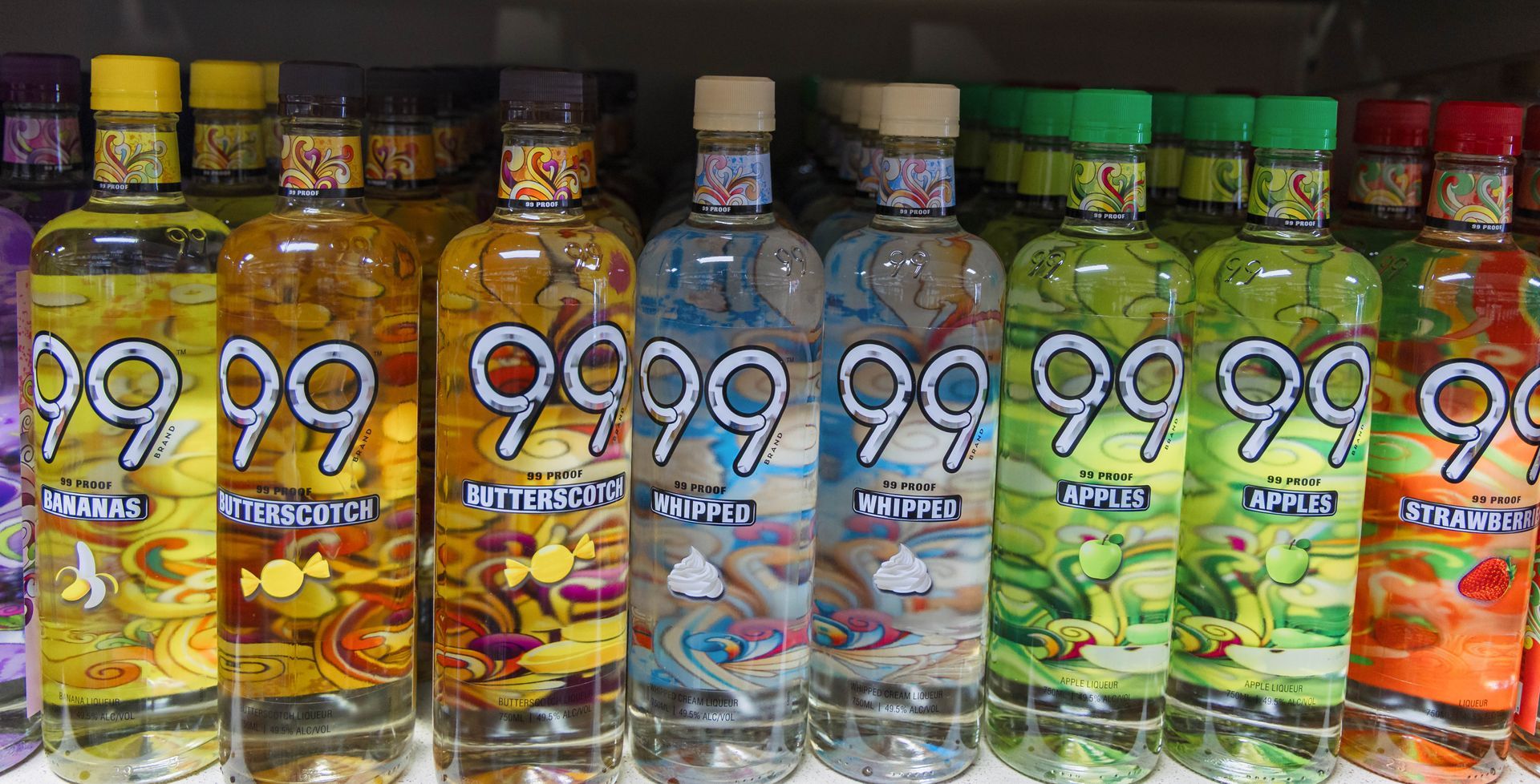 Bottles of 99 brand liqueur in various flavors: banana, peach, blue raspberry, apple, and strawberry.