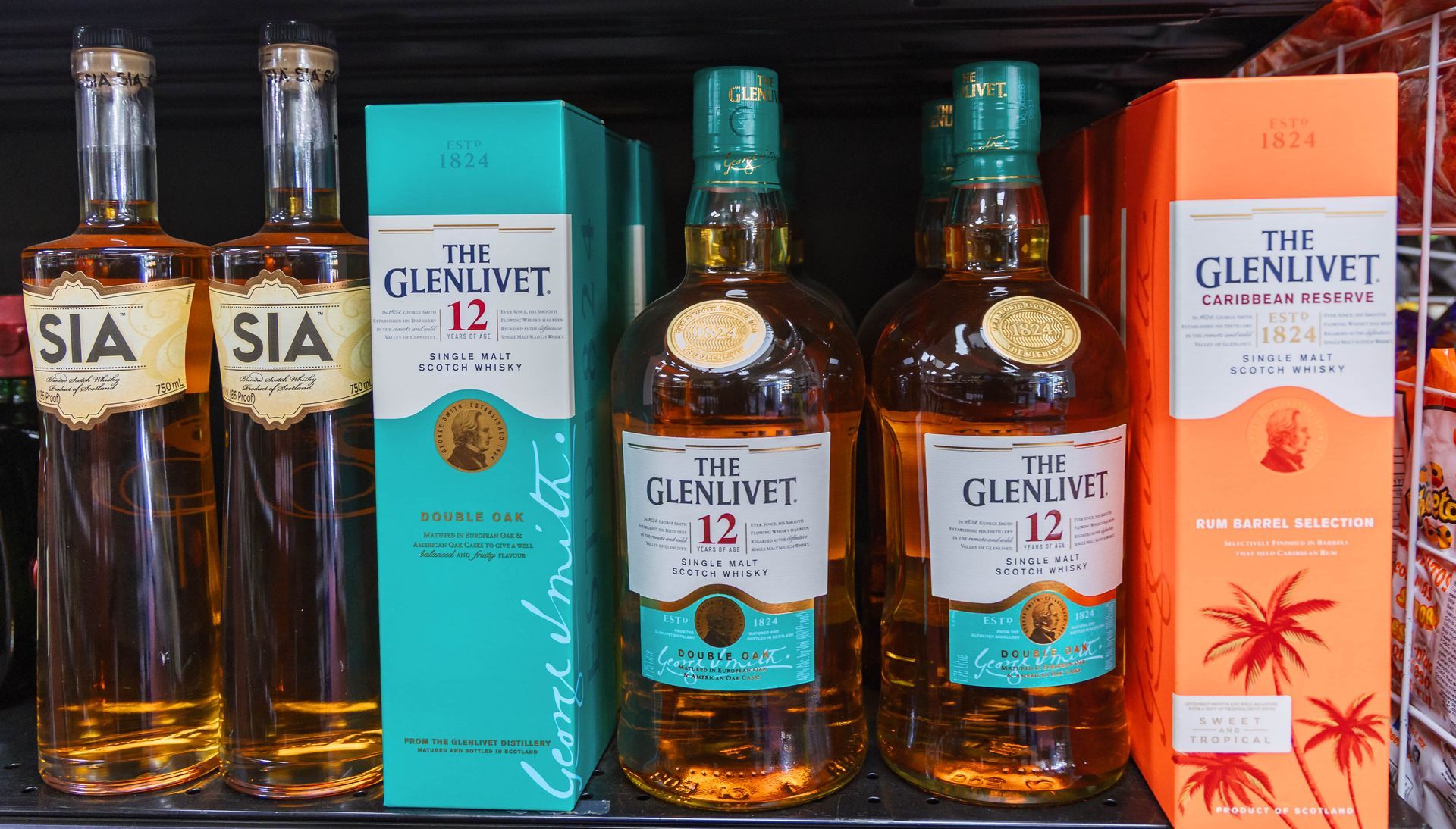 Whiskey bottles on a shelf: two SIA, two Glenlivet 12, and one orange boxed Glenlivet.