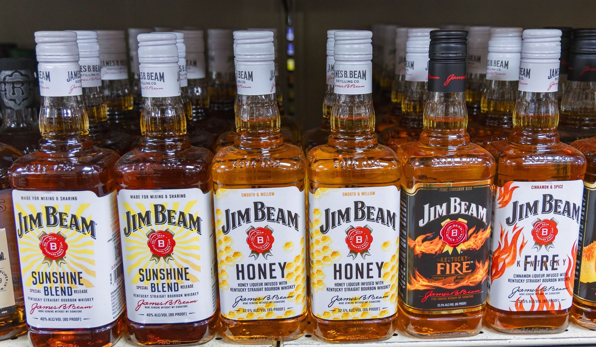 Bottles of Jim Beam flavored whiskey on a shelf, including honey, fire, and sunshine blend varieties.