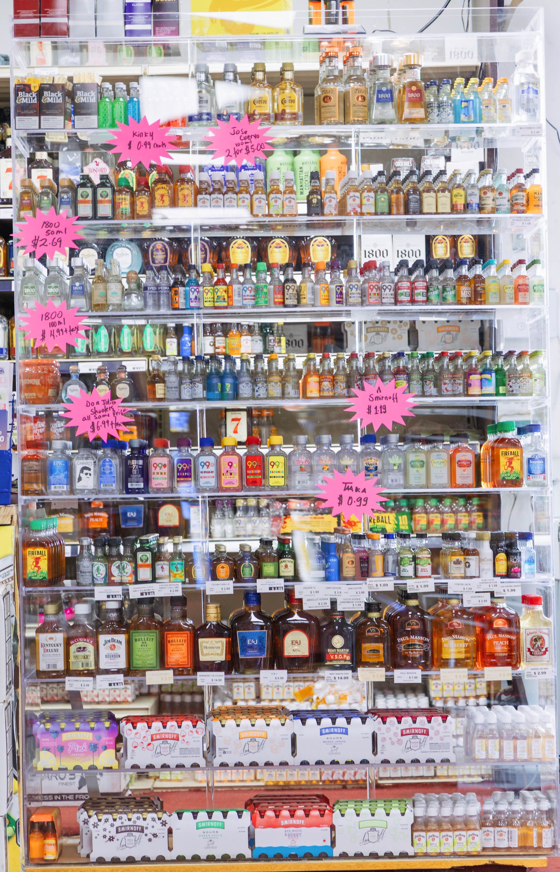 Liquor store display with various miniature bottles of alcohol, price tags visible.