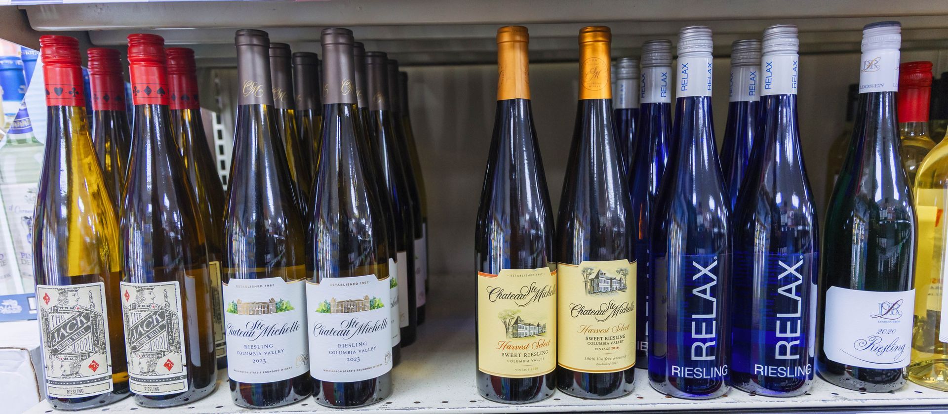 Bottles of wine on a store shelf, various colors, including red, yellow, and blue bottles with the word 