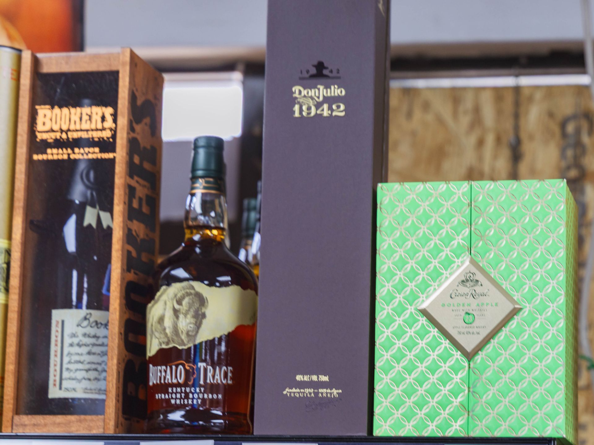 Liquor bottles on a shelf: Booker's bourbon, Buffalo Trace, Don Julio 1942, and a green-boxed bottle.