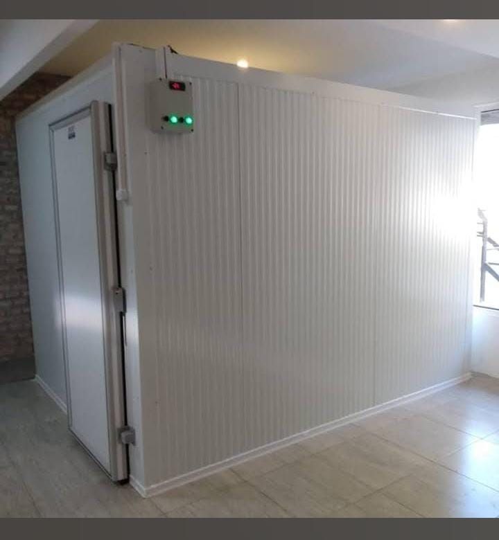 Habitación blanca aislada con puerta y pequeñas luces indicadoras verdes en un interior alicatado.
