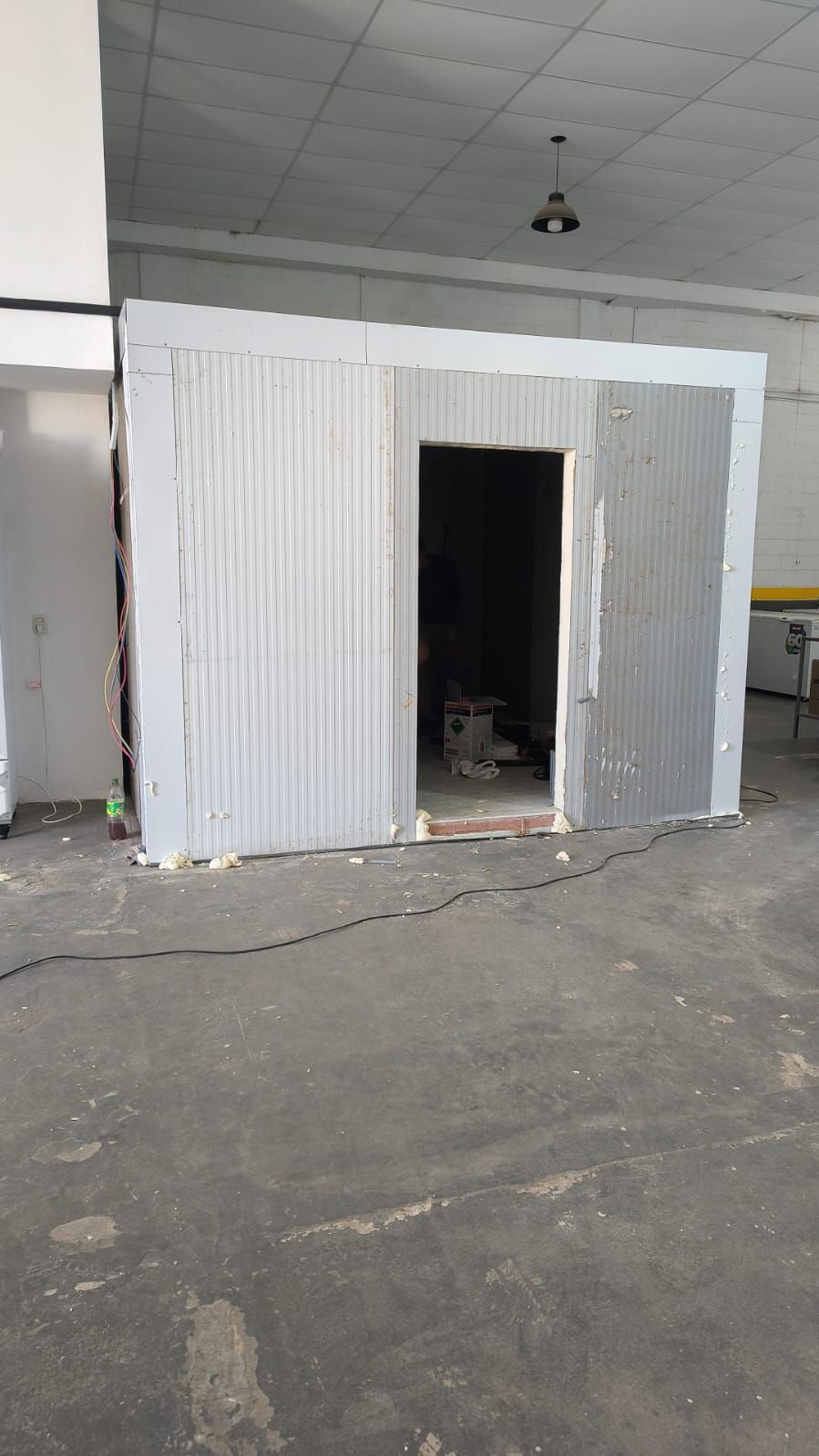 Pequeña estructura blanca de chapa ondulada, similar a un cobertizo, ubicada en un almacén