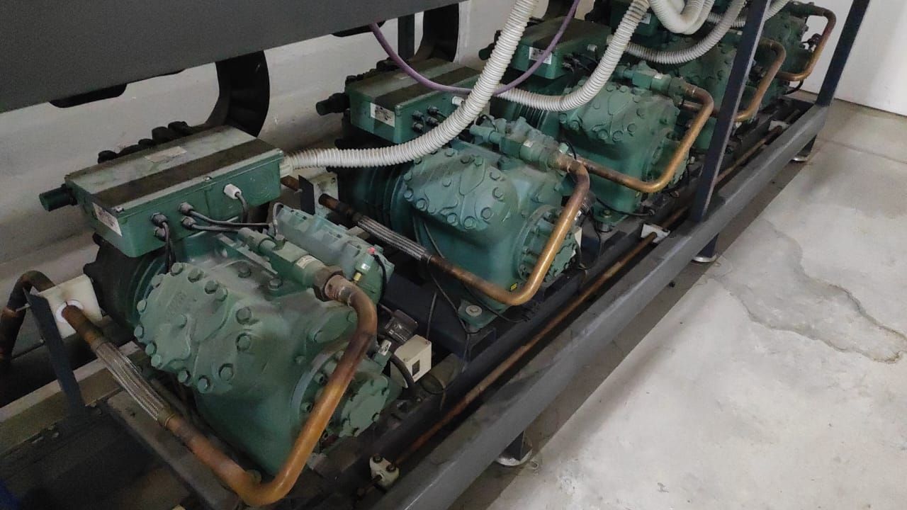 Compresores y tuberías industriales de color verde dentro de una sala de máquinas sobre una estructura metálica.