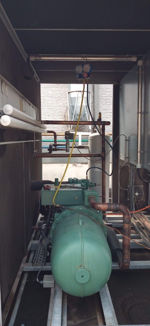 Depósito industrial verde y tuberías dentro de una estrecha sala de máquinas.