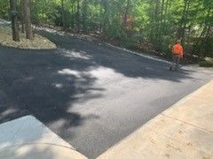 Freshly paved asphalt driveway with person in orange vest; trees in the background.