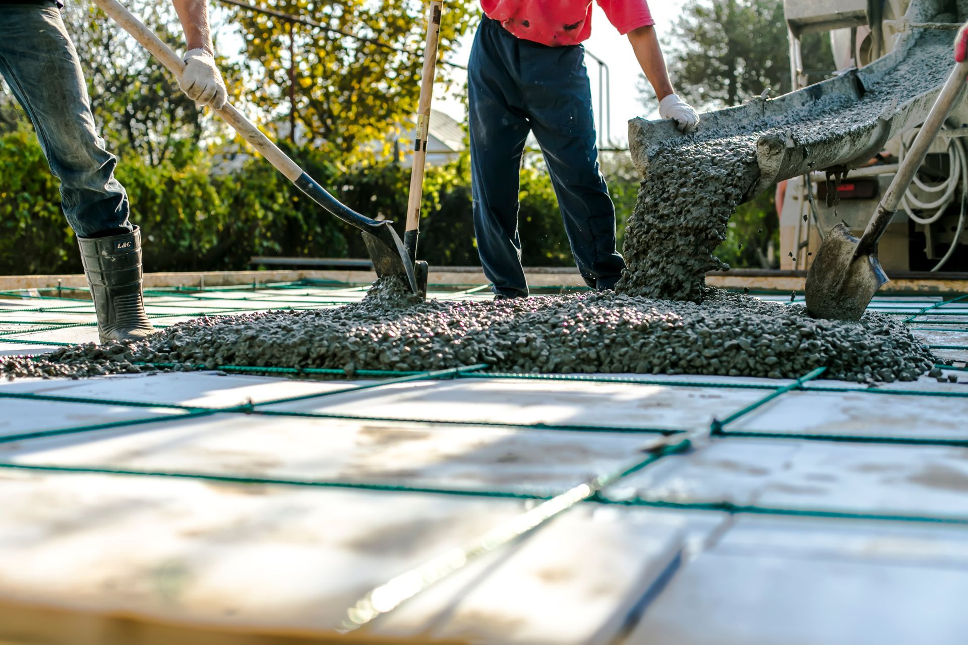 Workers spreading poured concrete over a reinforced surface at a construction site.