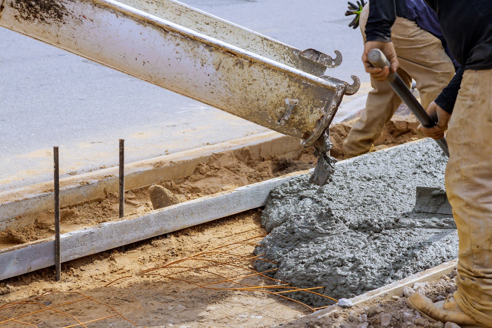 Concrete is poured from a mixer chute into a framed curb as workers spread wet cement