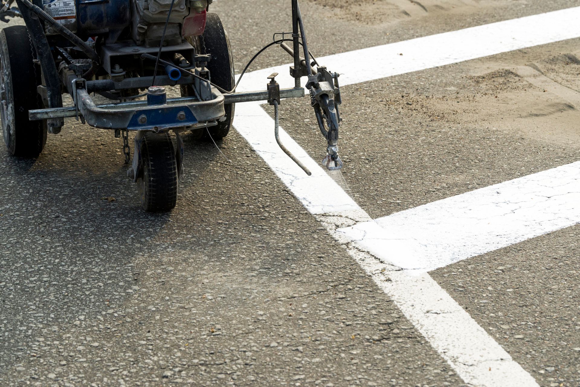 A small machine paints white road markings on asphalt near an intersection.