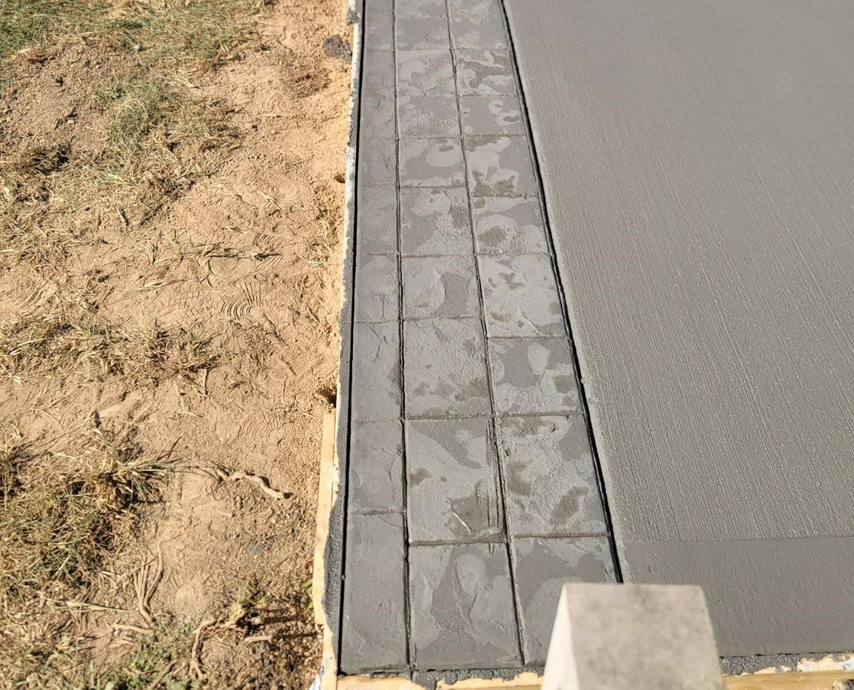Freshly poured concrete next to a strip of gray, square pavers, bordering grass.