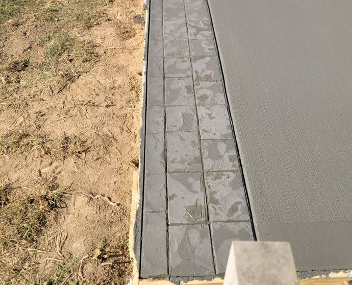 Freshly poured concrete next to a strip of gray, square pavers, bordering grass.