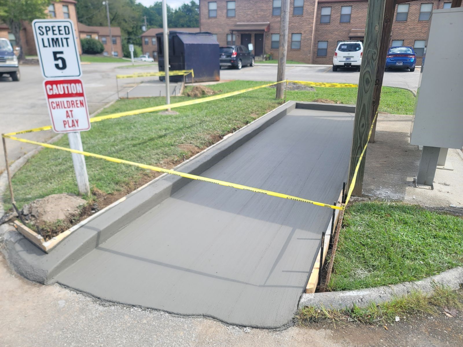 Newly poured concrete sidewalk with caution tape around it. Speed limit sign and building in the background.