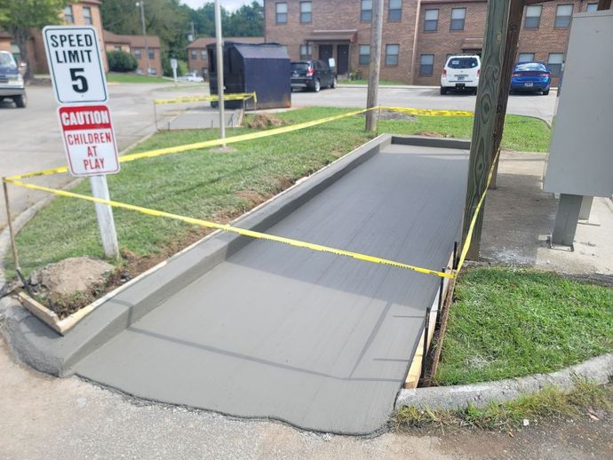 Newly poured concrete sidewalk with caution tape around it. Speed limit sign and building in the background.