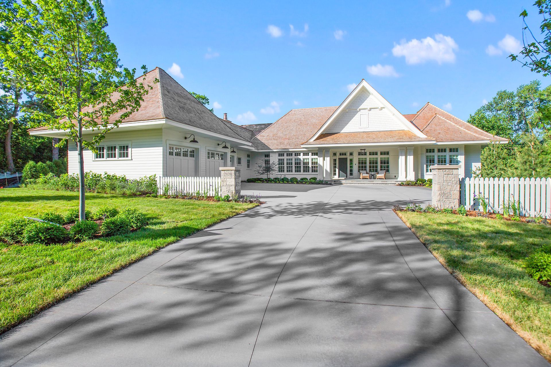 View of a white home with a smooth, wide concrete drive, done by a concrete driveway contractor.