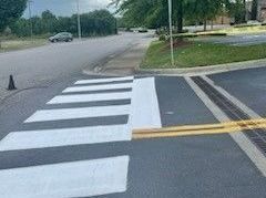 Crosswalk painted white on asphalt, near a grassy area and street.