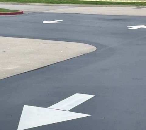 Asphalt parking lot with white directional arrows; a concrete curb on the left.