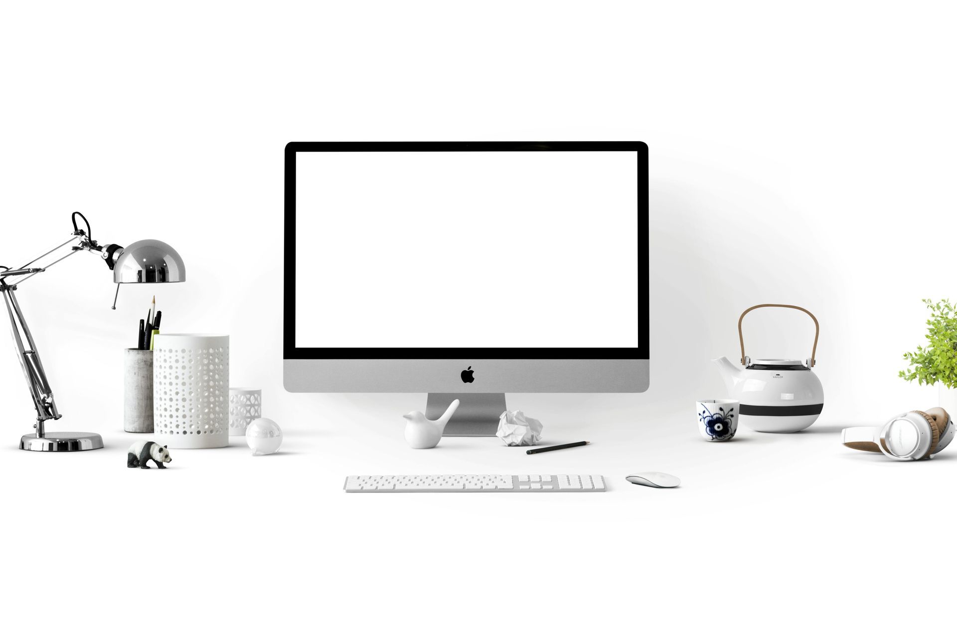 A desk showing a computer screen and keyboard with a lamp, a tea pot